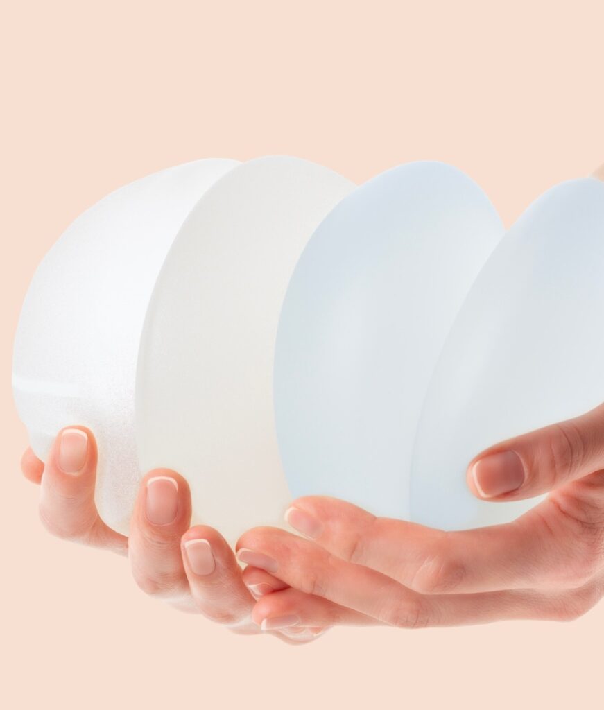Female hands holding stack of different types of breast implants.